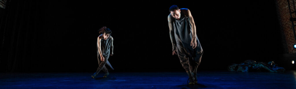 A male (Shinichi Iova-Koga) and female (Dana Iova-Koga) in mud and upside down grey hoodies, tipping sideways.